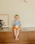 Smiling child in beanie holds mug and mushie Silicone Sensory Toy, coffee sign behind.