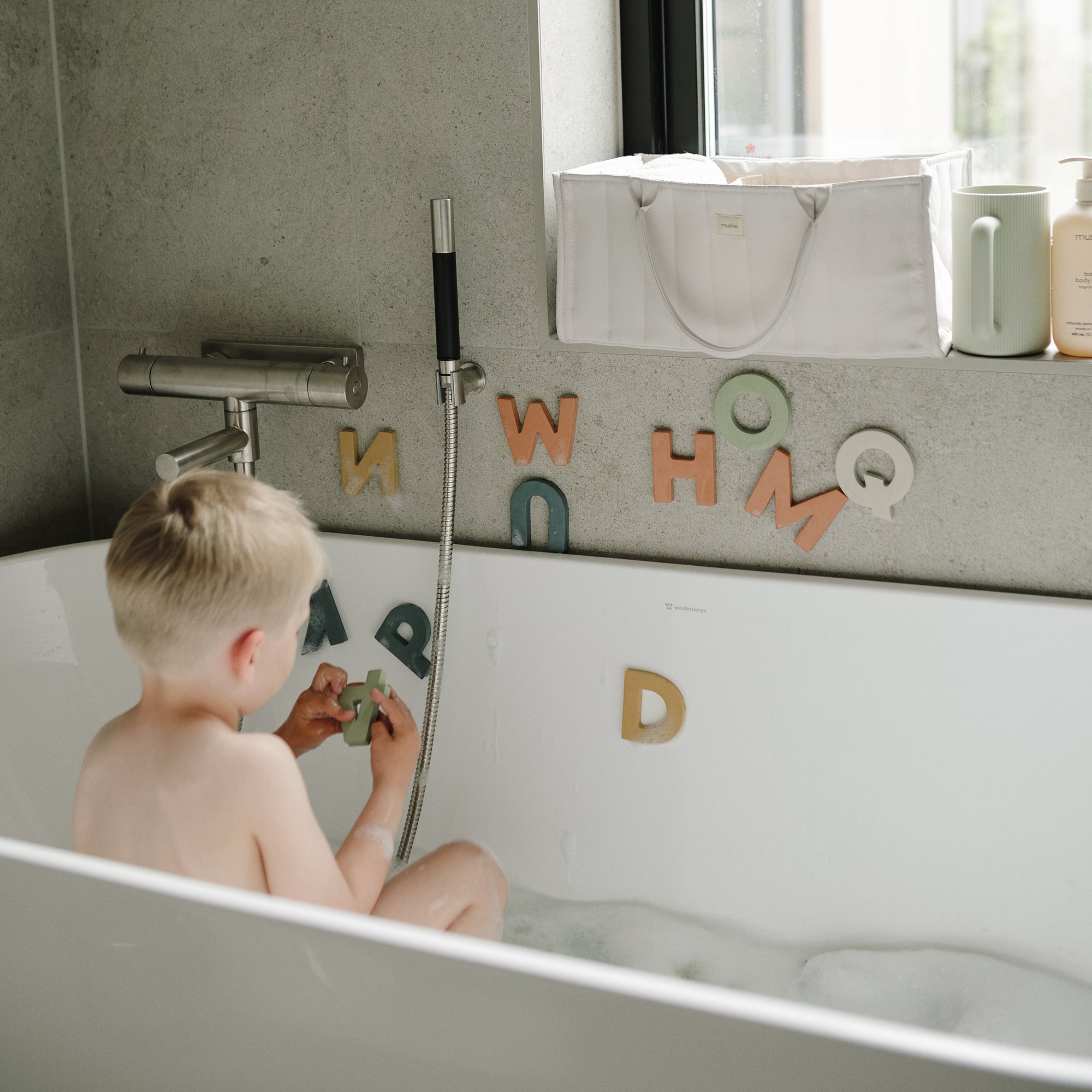 Young child playing with mushie Letters &amp; Numbers Bath Play Set in the bathtub.