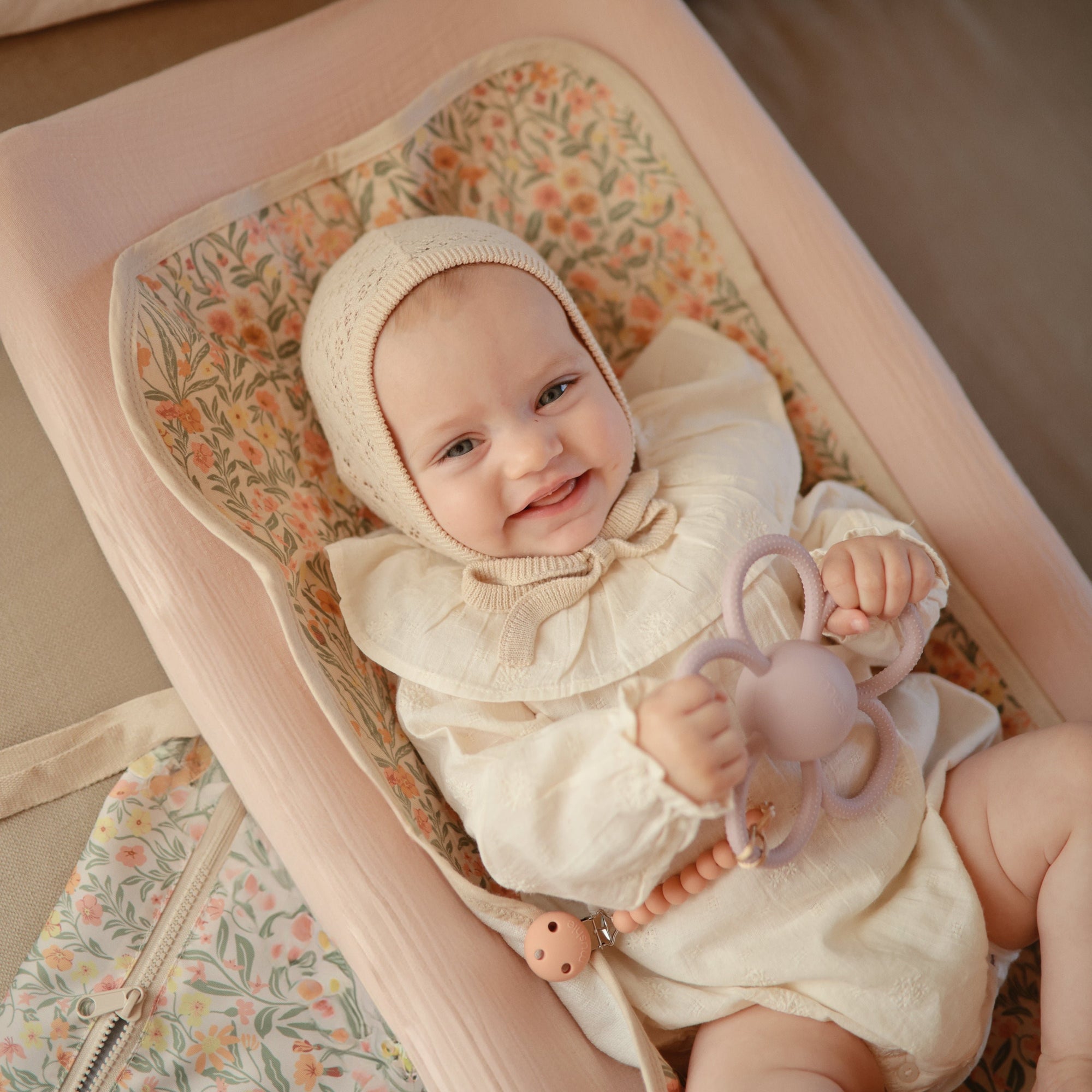 Baby on floral blanket with Mushie Changing Pad Liners, in cream bonnet and outfit.