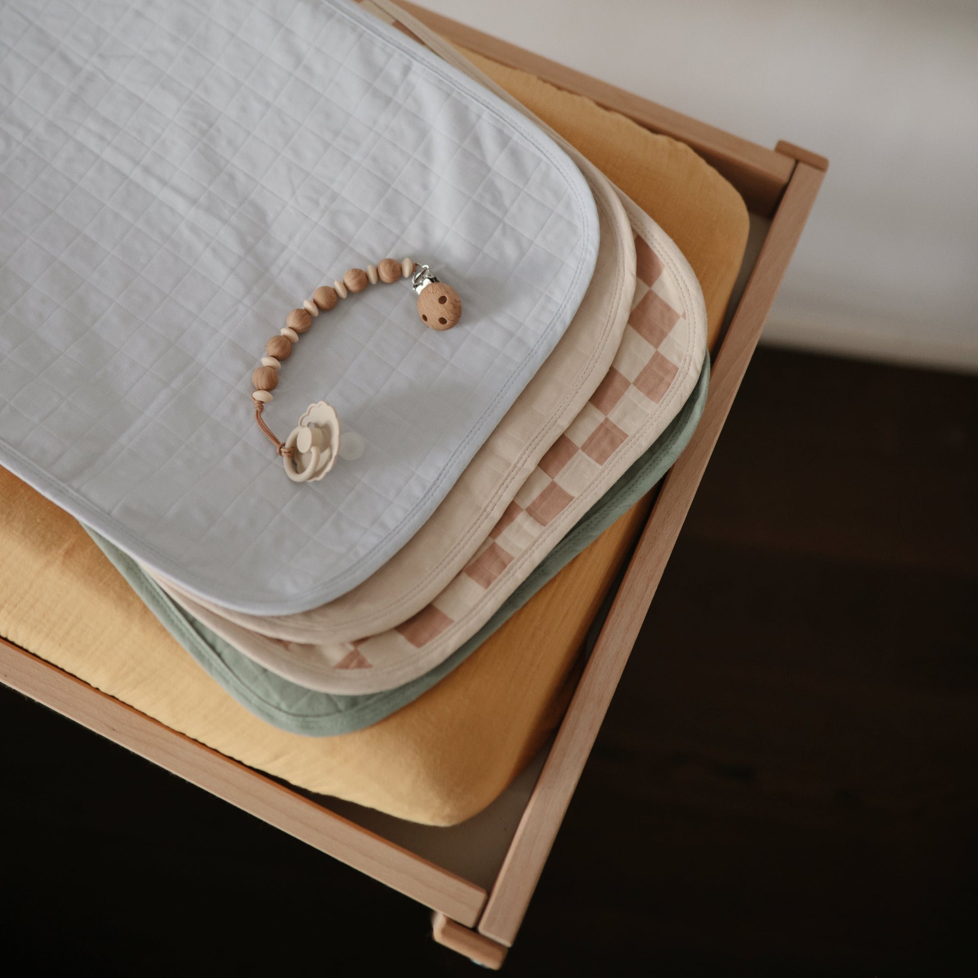 Mushie Changing Pad Liners stacked with a pacifier on a wooden changing table.