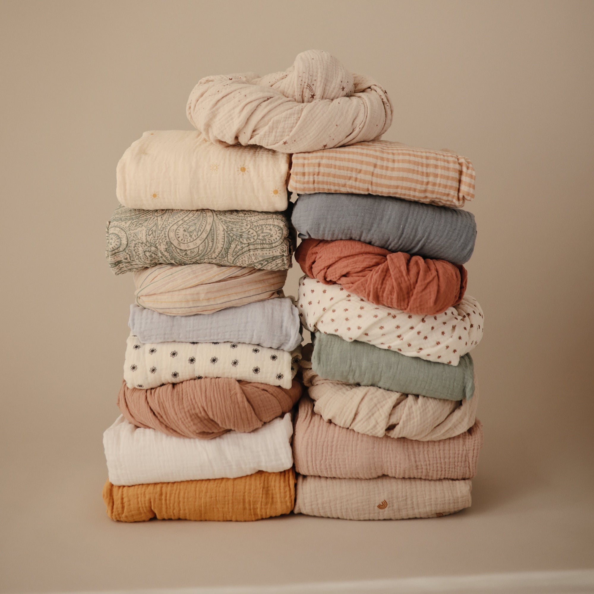 The mushie Mini Muslin Crib Sheet on a neutral background with colorful, textured baby bedding.