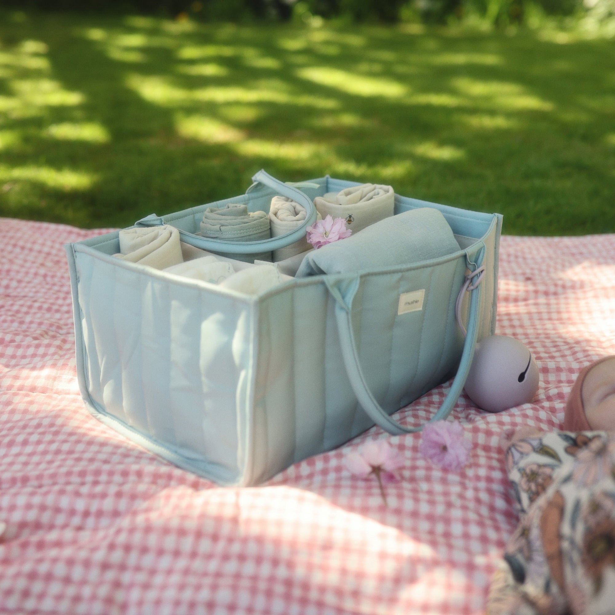 Mushie Changing Pad Liners in a light blue organizer on a pink picnic blanket outdoors.