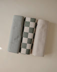 Three rolled Mushie Changing Pad Liners—green, checkered, beige—resemble organic cotton.