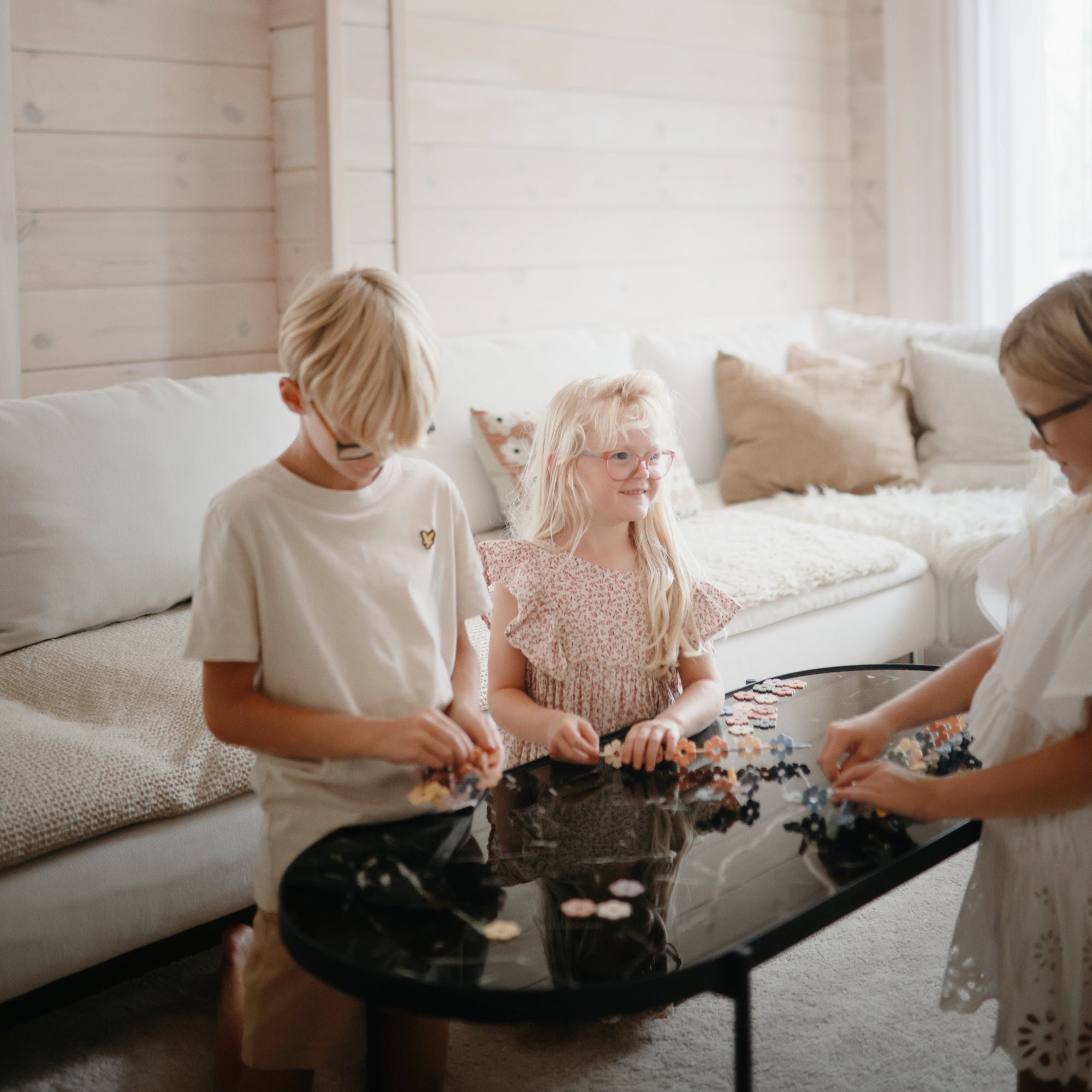 Three kids play with the mushie HEX Connect Building Toy Set on a black coffee table.
