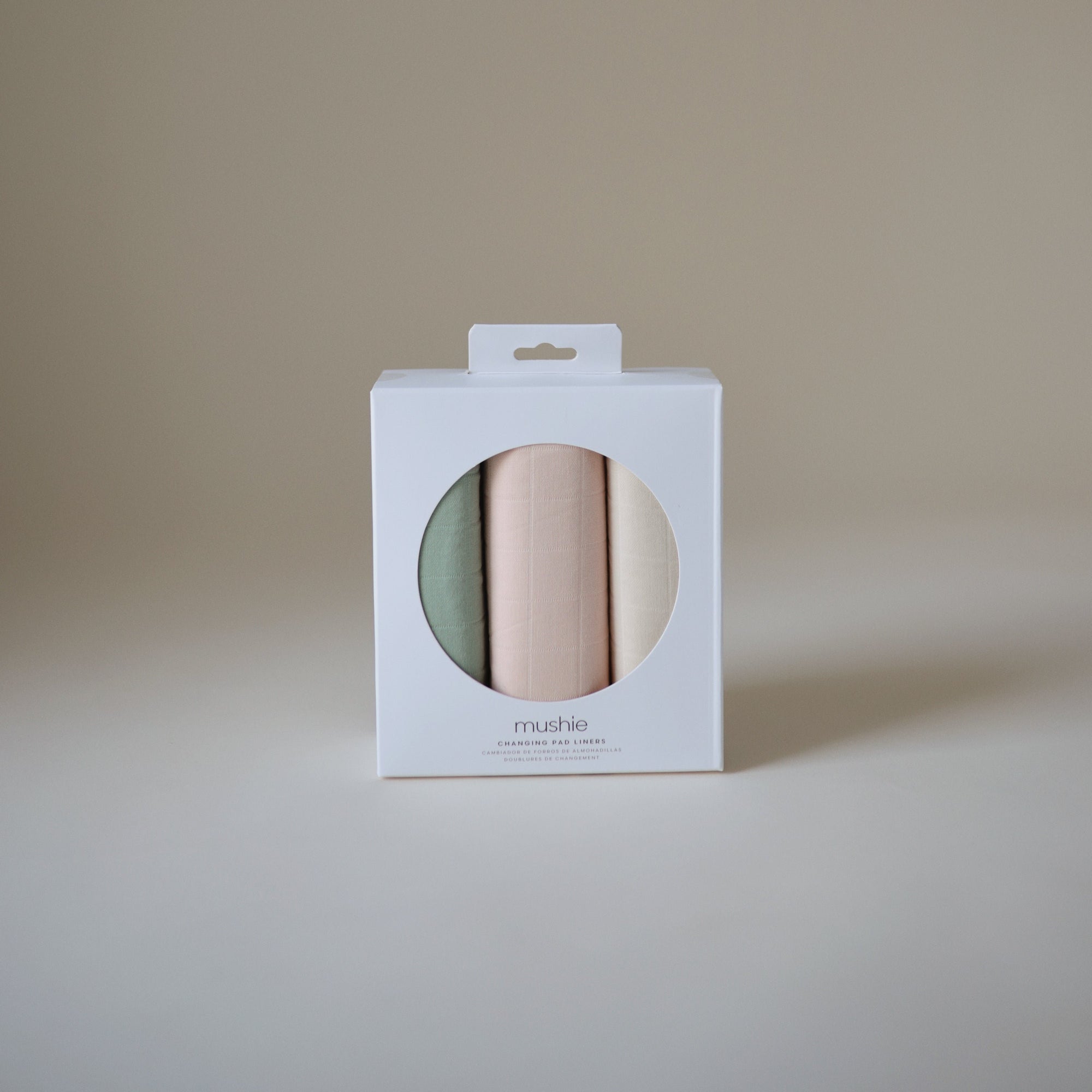 Mushie Changing Pad Liners—set of three organic cotton rolls in pastels, seen through window.