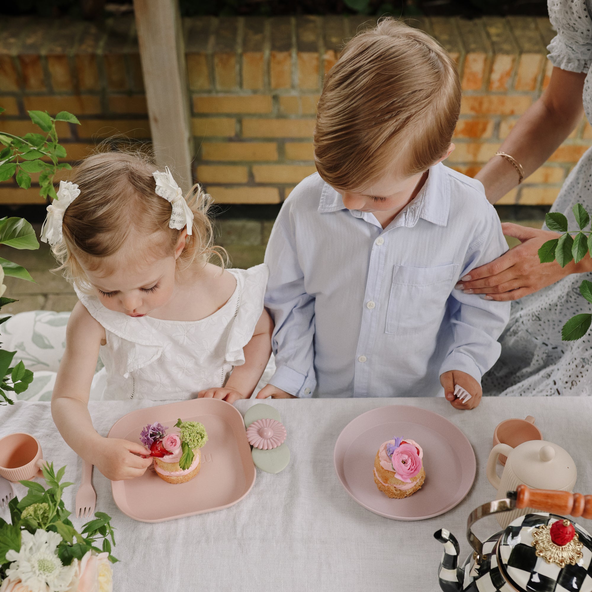 Two kids enjoy cakes and play with mushie Suction Spinner Toys at the table.