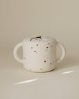 Beige mushie Snack Cup for toddlers with two handles, red and blue stars.
