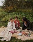A woman and two children sit outdoors with mushie Kaleidoscopes, eating marshmallows on sticks.