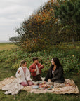 A woman and two children having a picnic with a mushie lunchbox on an outdoor blanket.