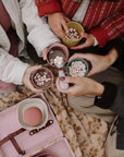 Four people holding colorful mushie Dinnerware Cups filled with hot cocoa and marshmallows.