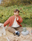 A young boy and a small white dog sit on a blanket with mushie Silicone Baby Food Containers.