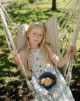 Girl with long blonde hair holds mushie Square Dinnerware Bowl in hammock, wearing glasses.