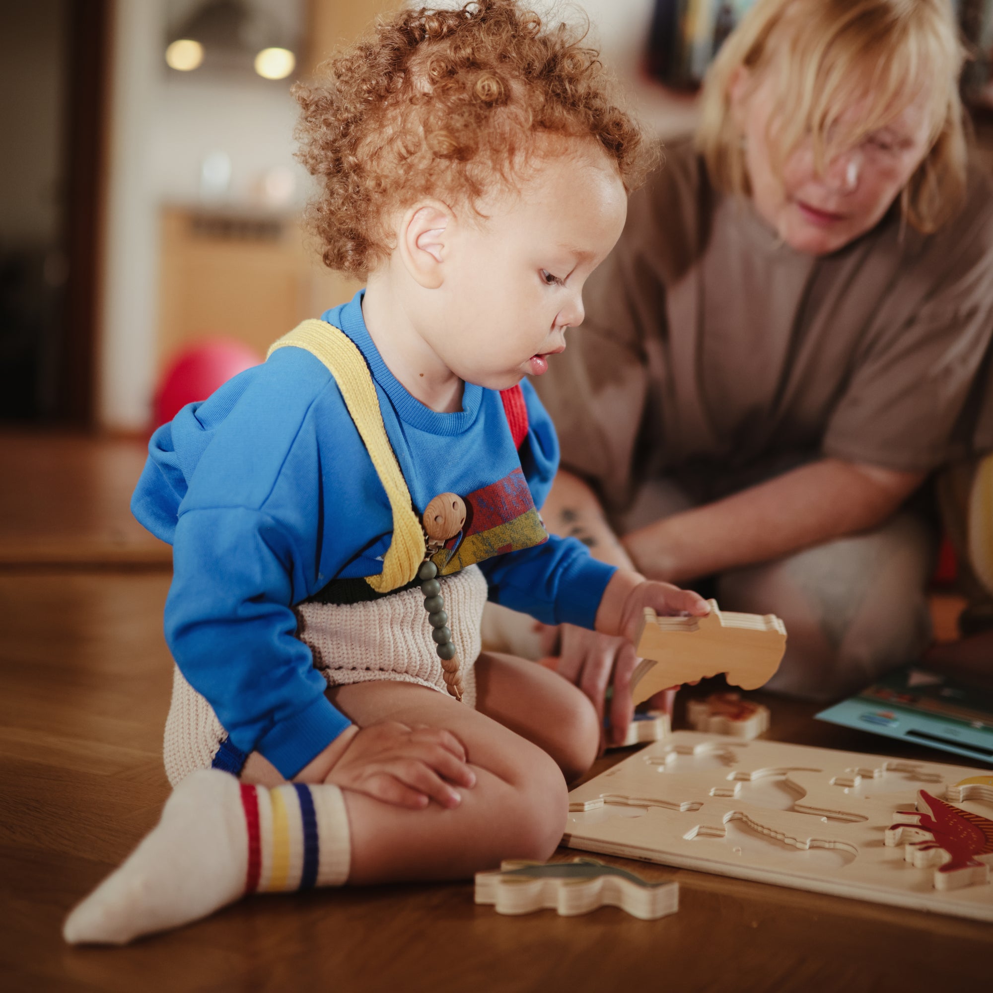 A toddler assembles a Mushie Wooden Puzzle as an adult assists with the FSC-certified toy.