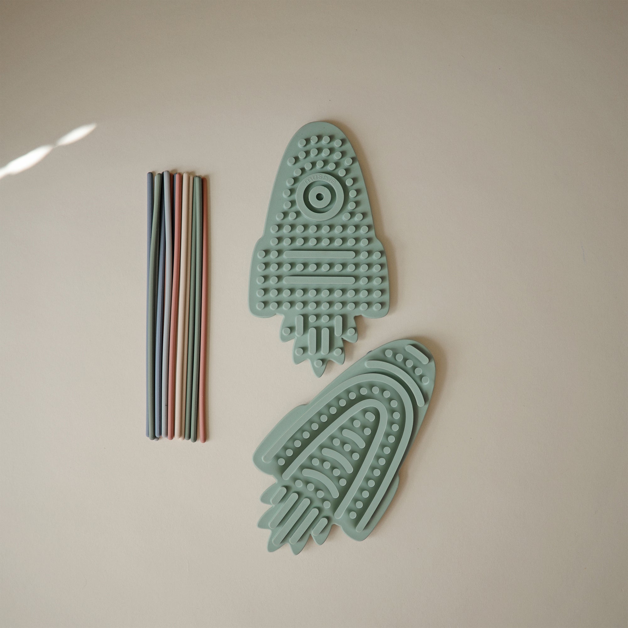 Two mushie Silicone Sensory Toys beside multicolored silicone straws for fine motor play.