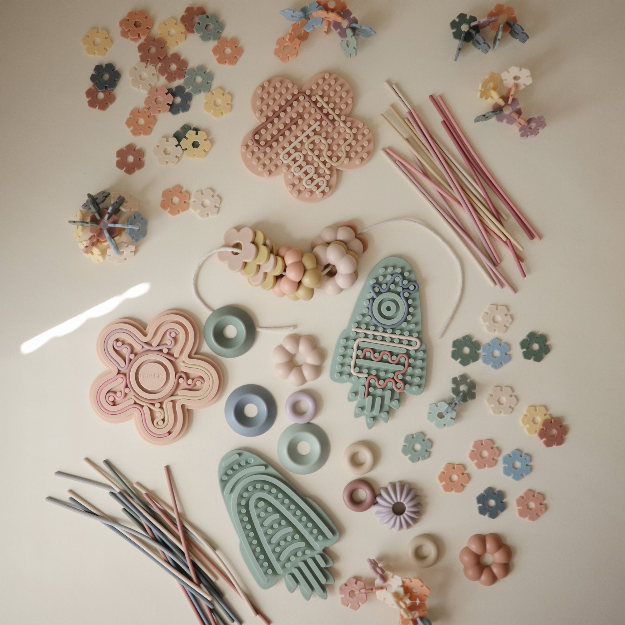 Mushie Silicone Sensory Toy and stacking rings enhance fine motor play on a light surface.