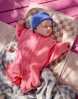 Baby on a mat with the mushie Organic Cotton Muslin Swaddle Blanket.