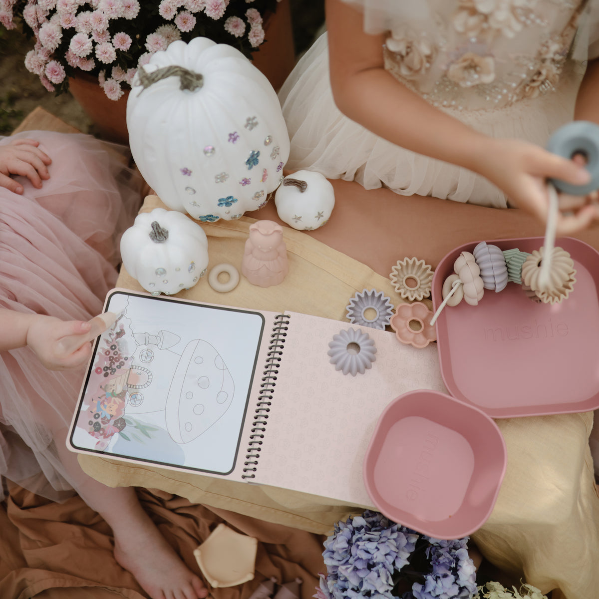 Kids use mushie’s Reusable Water Color Pad and play by pumpkins and flowers with pastel toys.