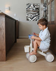 Young boy on a tricycle indoors, near a wooden counter with mushie Square Dinnerware Bowls.