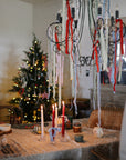 Festive table with Mushie Silicone Training Cup + Straw; Christmas tree lights glow behind.
