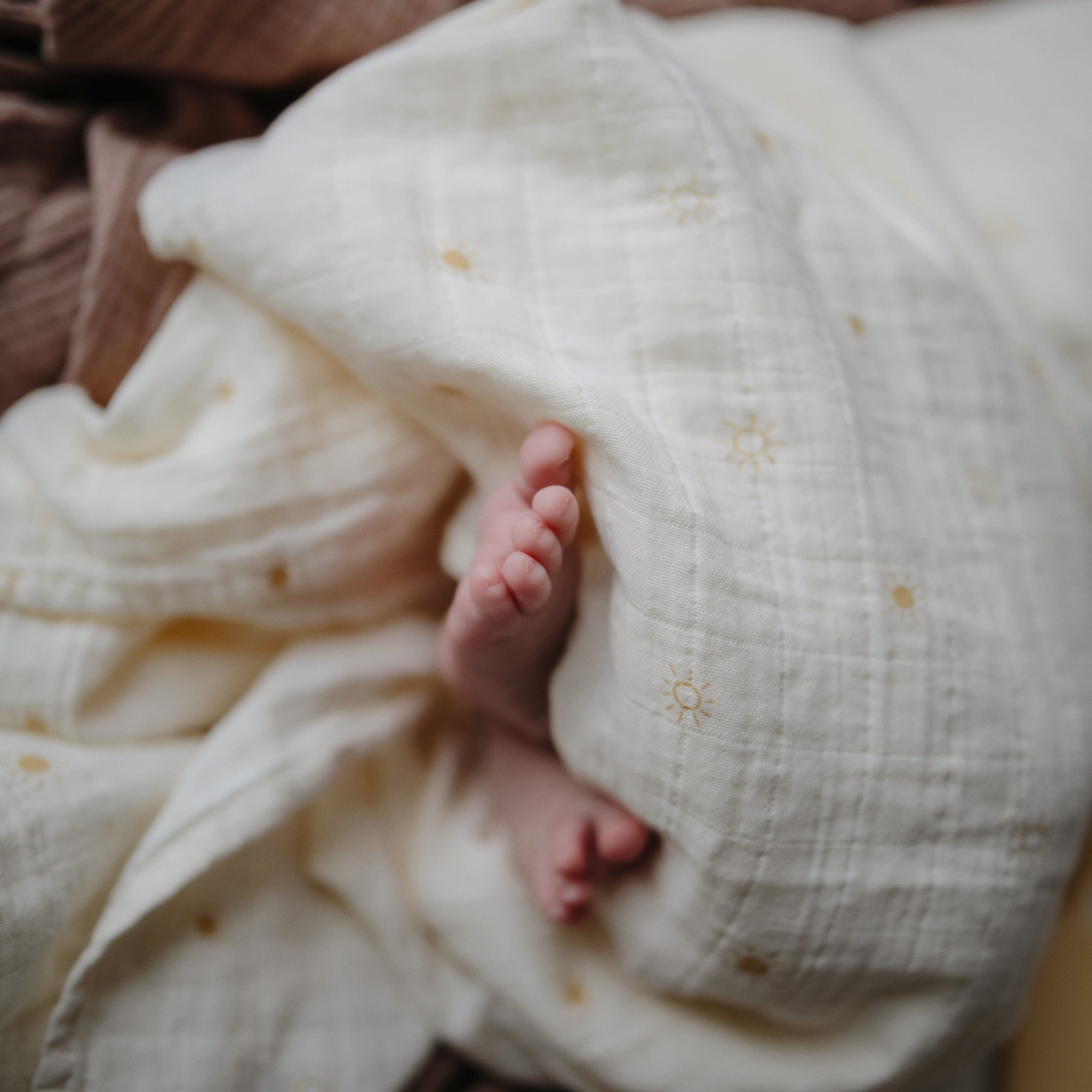 Lifestyle image of a baby swaddled in organic cotton swaddle in Suns
