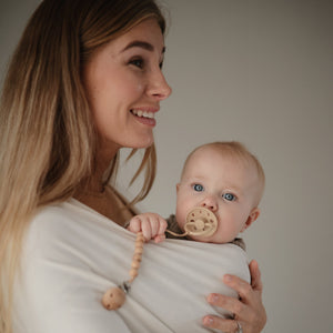 Lifestyle image of a mother and baby in the Mushie Baby Wrap with a Moon pacifier. 