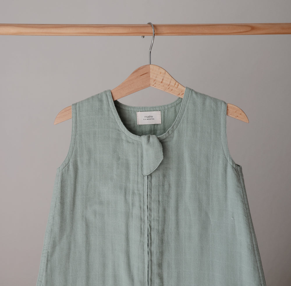 Lifestyle image of a Mushie Sleep Bag in Roman Green on a hanger.