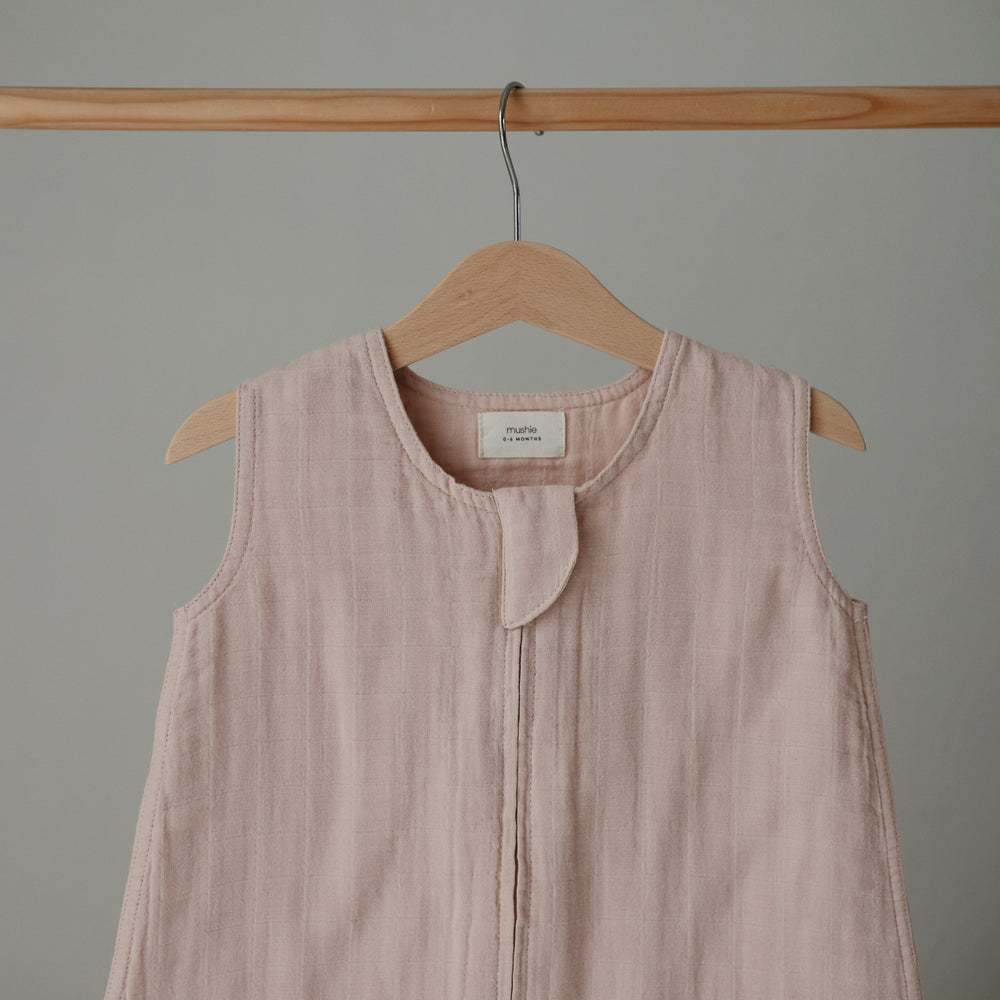Lifestyle image of a Mushie Sleep Bag in Blush on a hanger.