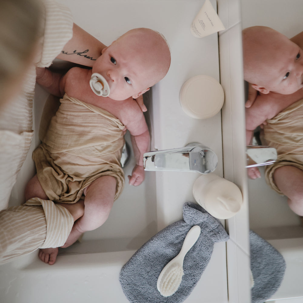 Lifestyle image of a bath mitt resting next to a baby.
